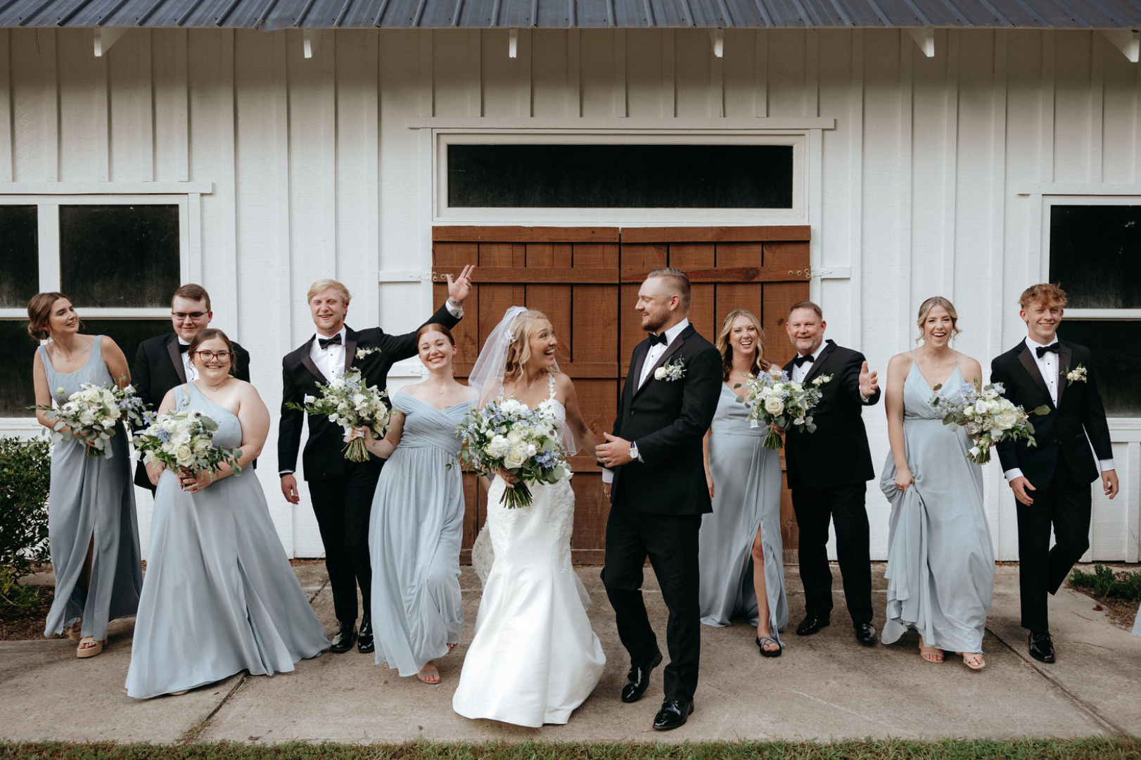 Bride and groom with wedding party outside white barn for joyful North Georgia wedding